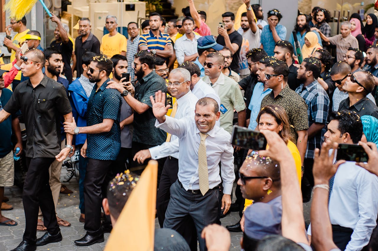 A politician waves to a crowd during a lively outdoor rally in a city street.